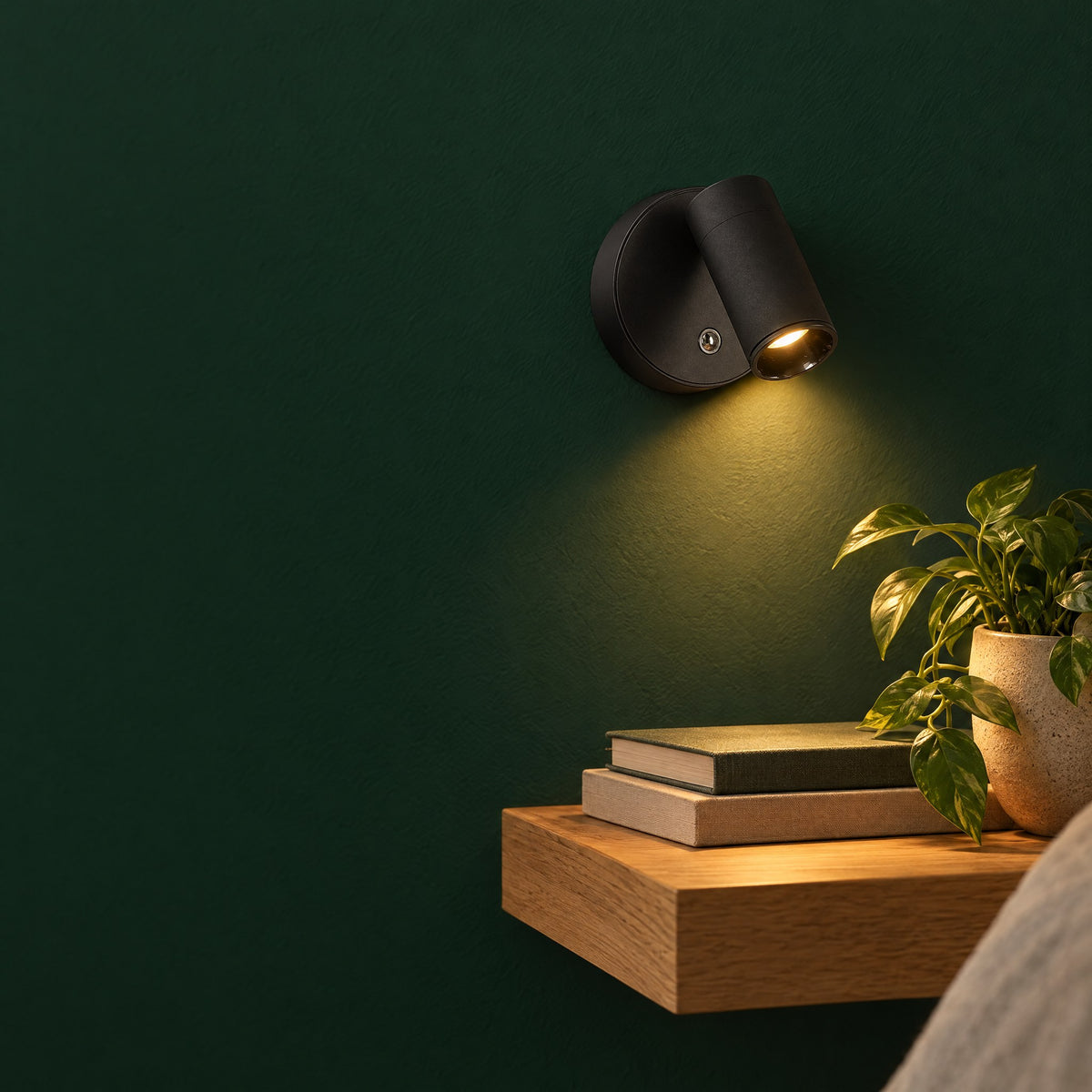 Cordless wall light on a green wall above a bedside shelf
